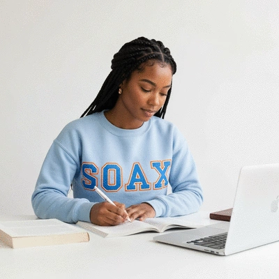 Young woman studying with textbooks and laptop, wearing sorority letters on a sweatshirt, symbolizing academic and sorority life balance, no text, no words, no typography, clean image